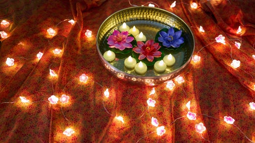 Diya decorations floating in water in a golden bowl on table filled decorated with a garland of twinkling lights